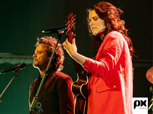 Een vrouw op een gitaar samen met een man bij de microfoon