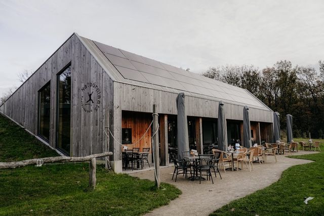 Ein Holzgebäude, das sich teilweise in einen grünen Hügel einfügt und dem eine Terrasse vorgelagert ist.