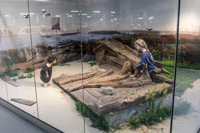 De resten van een Romeins houten schip met twee poppen erbij die  kinderen verbeelden.