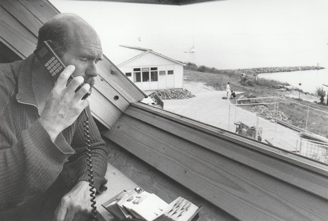 Een man telefoneert vanaf Pampus naar het vasteland. Hij staat in het dakraam van de enige woning op het eiland en kijkt uit over het water.