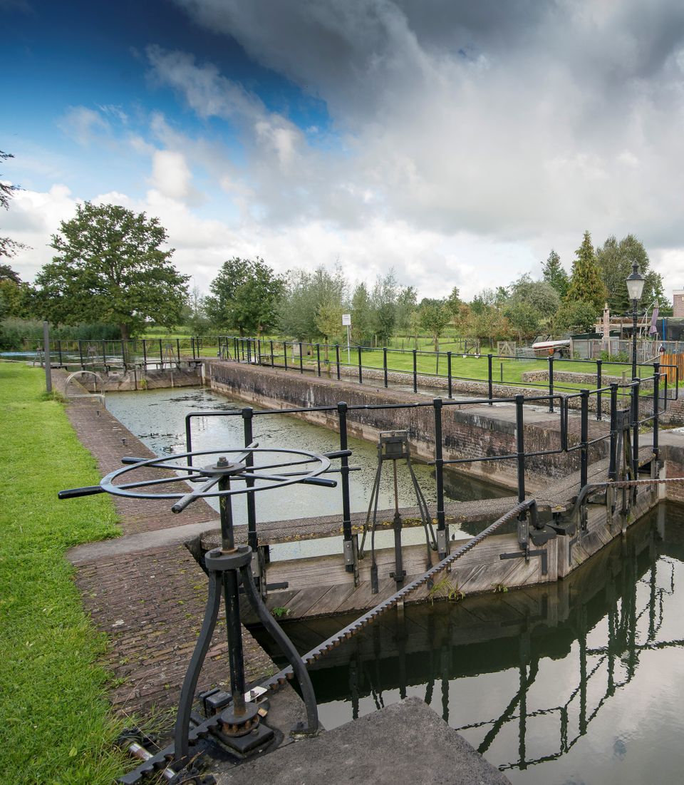 Een sluis van zwart metaal en bakstenen in een groene omgeving.