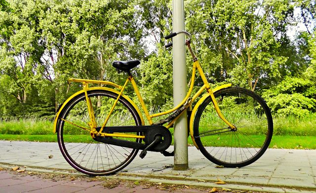 Een gele fiets staat vastgebonden aan een lantaarnpaal.