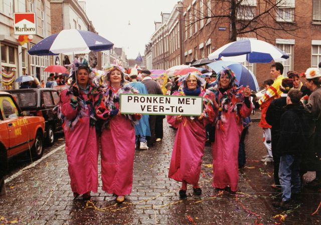 Vier vrouwelijke deelnemers in het paars met bord: "Pronken met veer-tig", tijdens intocht 1990.