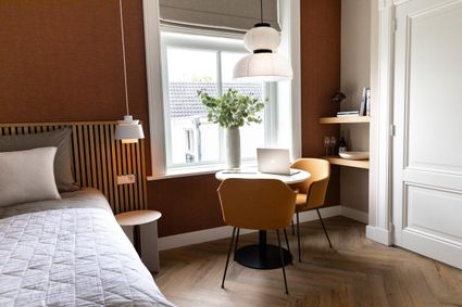 Moderne hotelkamer van Boutique Pastorale in Montfoort met comfortabel bed, ronde tafel met stoelen, werkplek bij het raam en warm interieur in aardetinten.