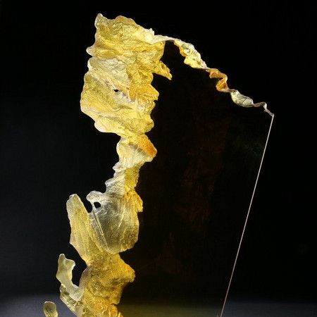 Geel-goudkleurig glassculptuur met een donkere achtergrond.