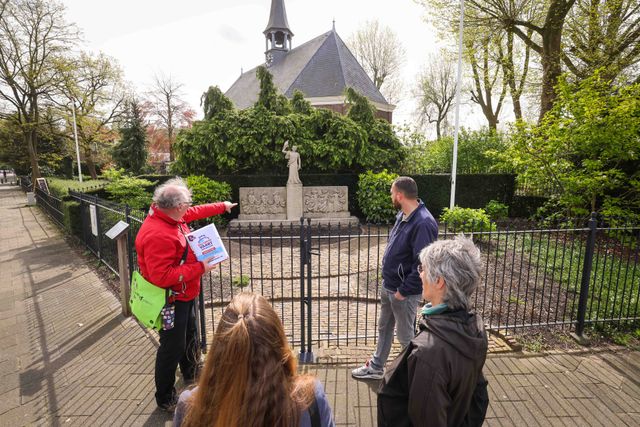 Gids wijst naar het herdenkingsbeeld in Jutphaas, er staan een paar mensen te luisteren naar zijn verhaal.