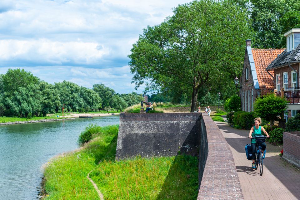 Een vrouw op een fiets fietst langs de vestingwal van een oud stadje.