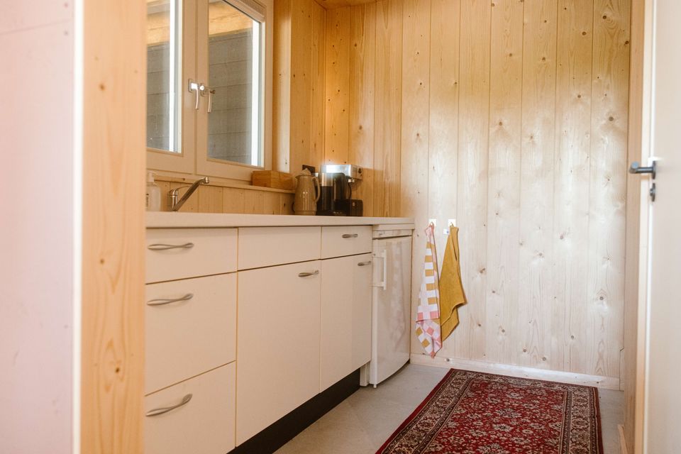 Keuken van Aliedas Annex bij Esti Yoga in Lopik, Groene Hart, met lichte houten wandbekleding, witte keukenkasten, koffiezetapparaat en koelkast.
