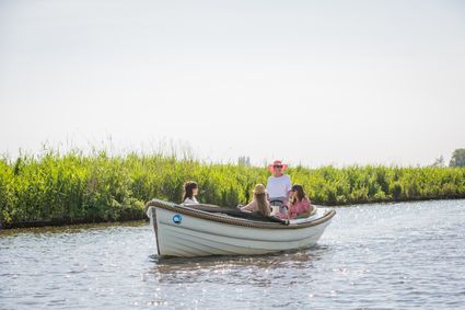 Vier vrouwen varen in een sloep langs weilanden.