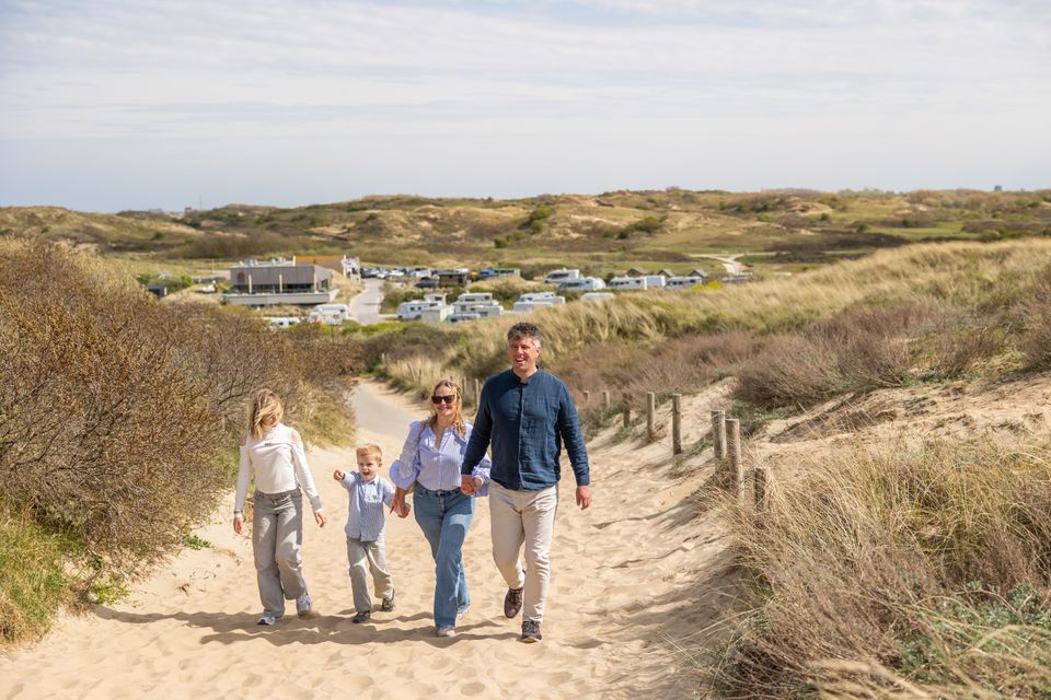 Een gezin loopt het duin op richting zee in Katwijk, met op de achtergrond Strandcamping Zuidduinen in beeld.