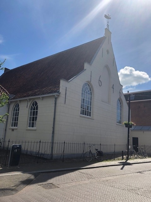 De Lutherse Kerk in Woerden met bouwjaar 1646 op de gevel, witte muren, hoge ramen en een zonovergoten dak met windwijzer in de vorm van een zwaan.