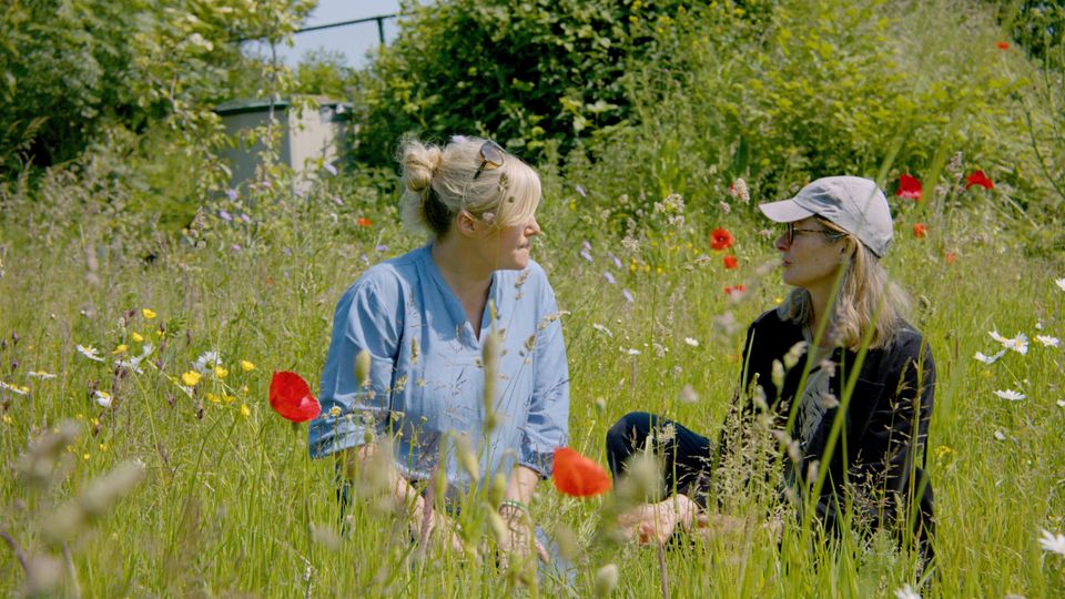 Twee vrouwen zitten in het hoge gras tussen de wilde bloemen.