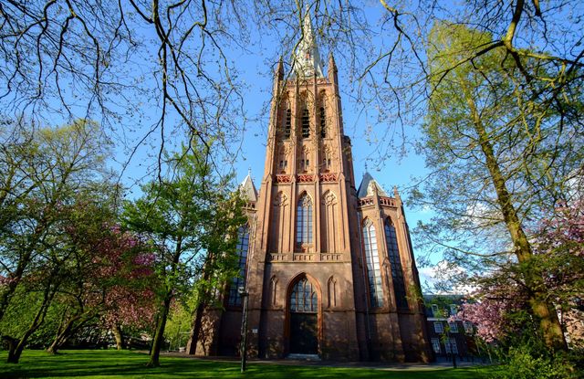 Kerk Sint-Nicolaasbasiliek IJsselstein, Groene Hart, neogotische basiliek met hoge kerktoren, omringd door bloeiende bomen en groen stadspark op een zonnige lentedag.
