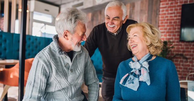 Oudere dame en twee oudere heren praten en lachen met elkaar