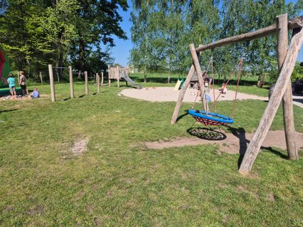 Schommel in speeltuin met op achtergrond een glijbaan de 3 kinderen