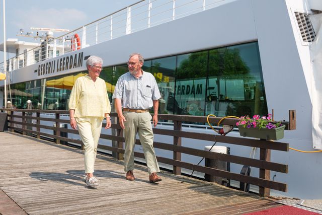 Twee personen lopen over een bruggetje met op de achtergrond Rederij Leerdam