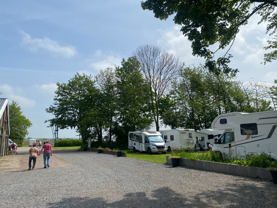 Een foto van een camping met 2 mensen op de voorgrond en een aantal campers op camperplaatsen.