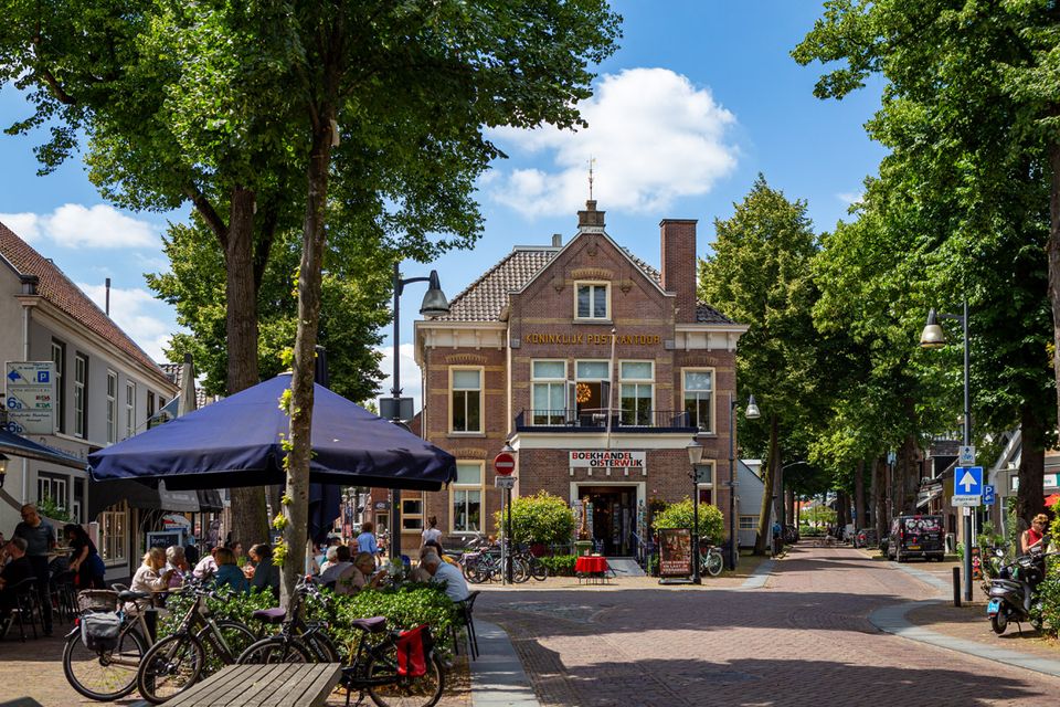 Monumentaal pand van het Oude Postkantoor in de zomer, met op de voorgrond een vol terrasje