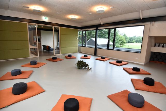 Een lichte ruimte met op een witte vloer oranje matjes en zwarte kussentjes.