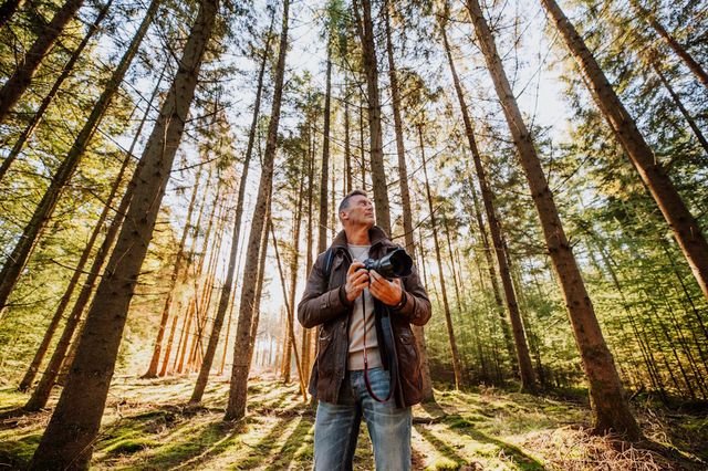 Een man staat met zijn fotocamera in de natuur in Drenthe en kijkt om zich heen.