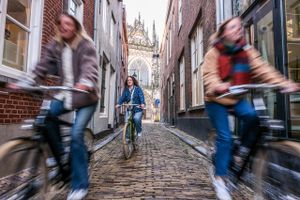 Meiden fietsen door steegje in 's-Hertogenbosch met doorkijkje op Sint-Janskathedraal