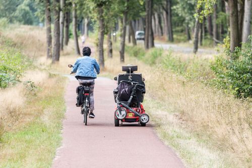 Een scootmobiel en fiets op een fietspad in de natuur.