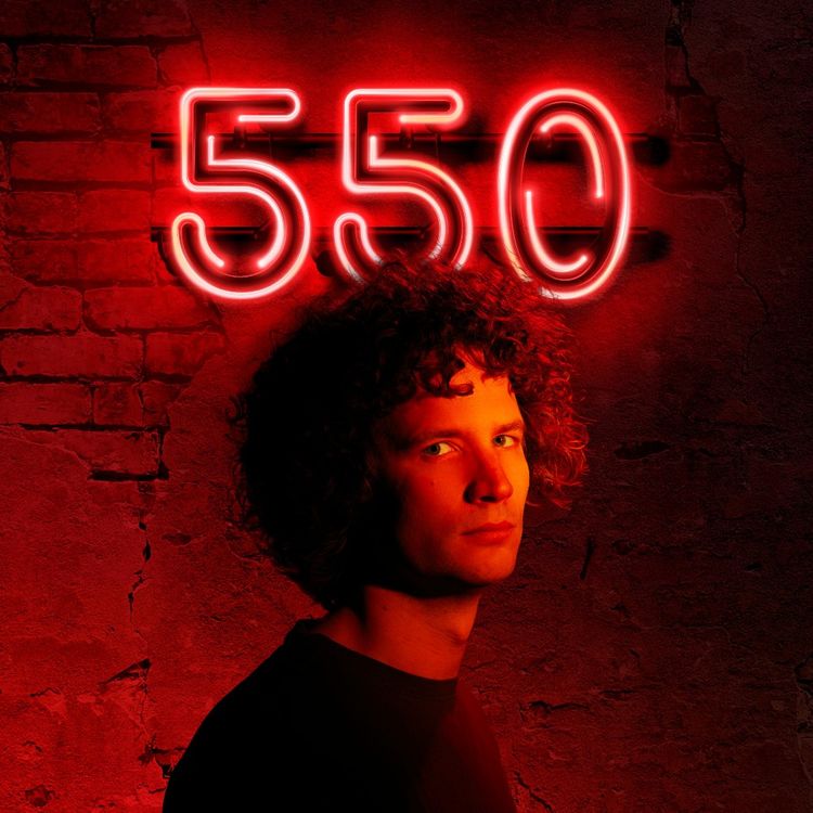 Foto van Tim voor een muur met rood verlichte cijfers 550, waardoor de foto een rode gloed heeft.