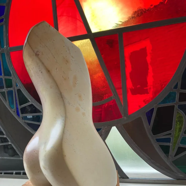 Beeldhouwwerk in de vorm van een witte torso tegen een glas in loodraam met rood als hoofdkleur