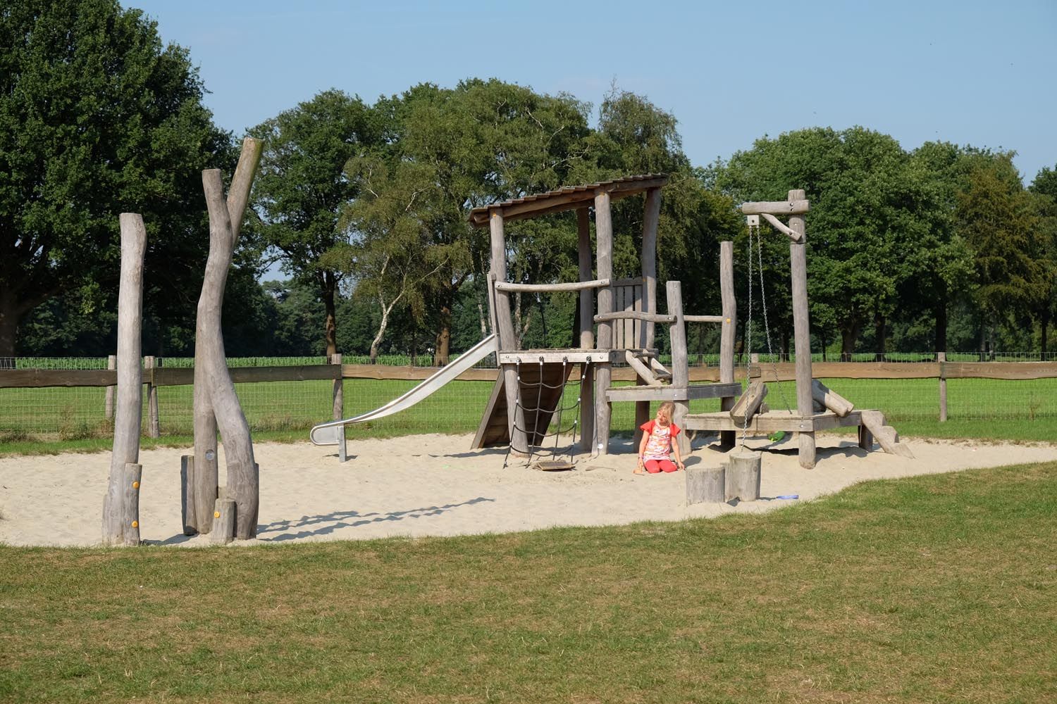 Kinderspeelplaats van De Gerrithoeve, houten klimtoestel in wit zand, omgeven door grasveld en bomen.