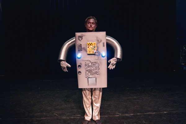 Theatervoorstelling Matinee met Diederik Jekel bij Het Klooster Woerden, stad Woerden, Groene Hart, persoon op het podium gekleed in een robotachtig kostuum tijdens een wetenschappelijke en humoristische voorstelling.