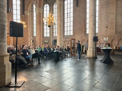 Foto van publiek in de Grote of Bartholomeüskerk in Schoonhoven. Rechts in de foto staat spreker Thijs de Groot van NBTC.