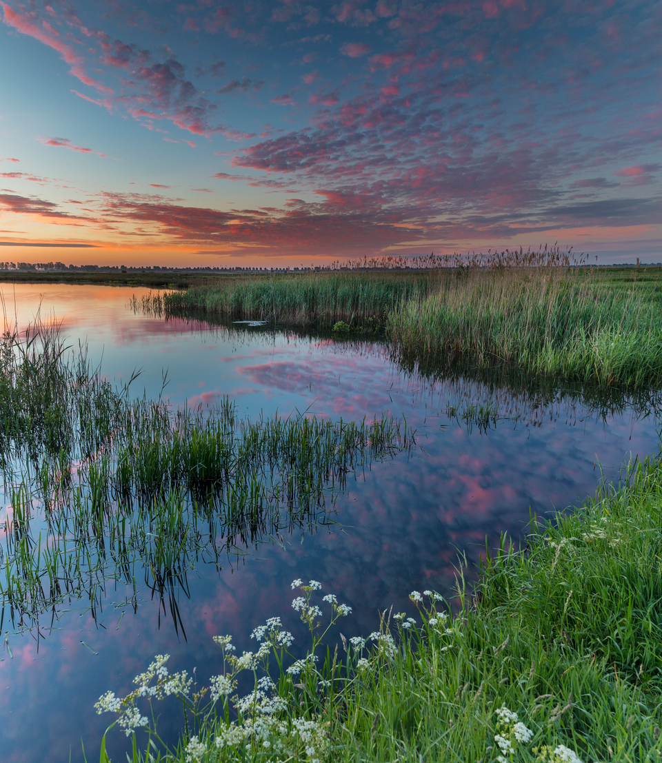 Einer der vielen Seen im hunzegebiet. Rosa Wolken spiegeln sich im Wasser. Das Gras an der Seite ist hellgrün.