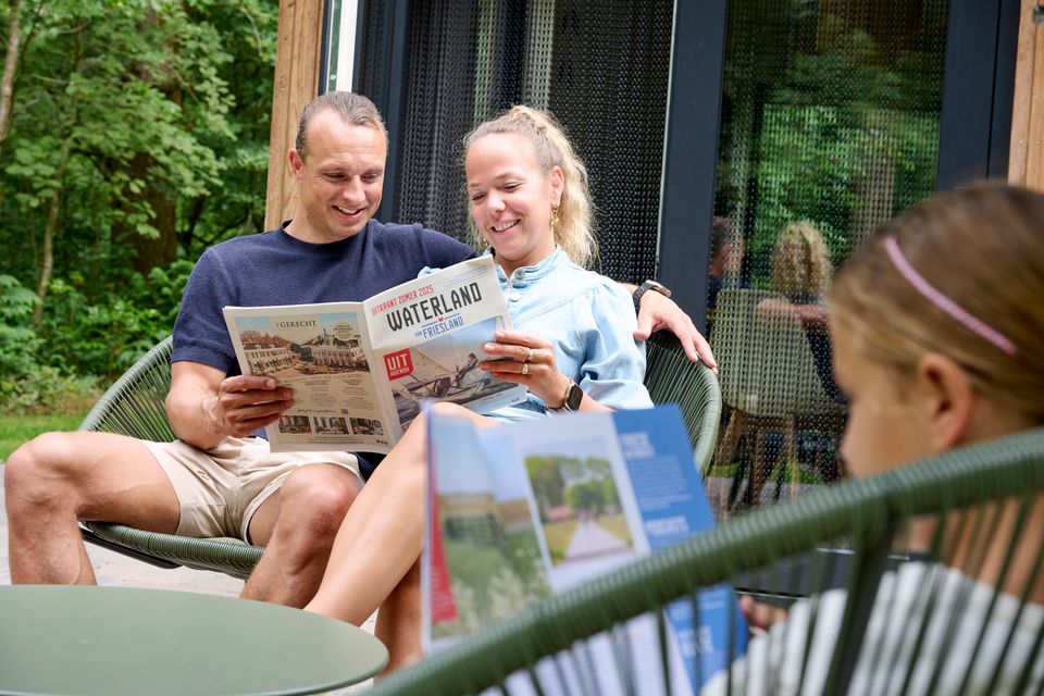 Een stel leest samen de Uitkrant van VVV Waterland van Friesland en op de voorgrond zit een meisje in het Inspiratiemagazine te lezen.