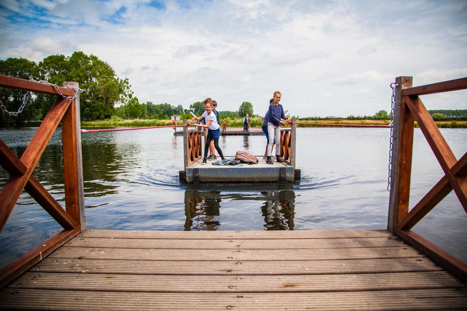 Een groep kinderen staat op een houten vlot op het water en trekken zichzelf naar de overkant.
