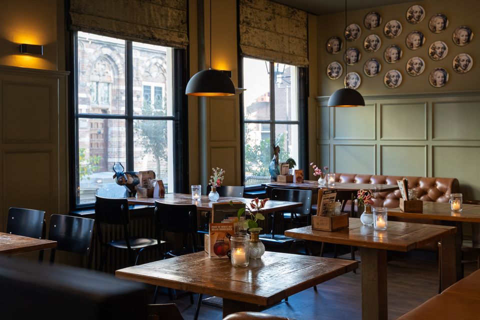 Restaurant Plein 7 in Woerden, Groene Hart, sfeervol restaurantinterieur met houten tafels, leren zitbanken, hanglampen, kaarslicht en decoratieve wandborden.