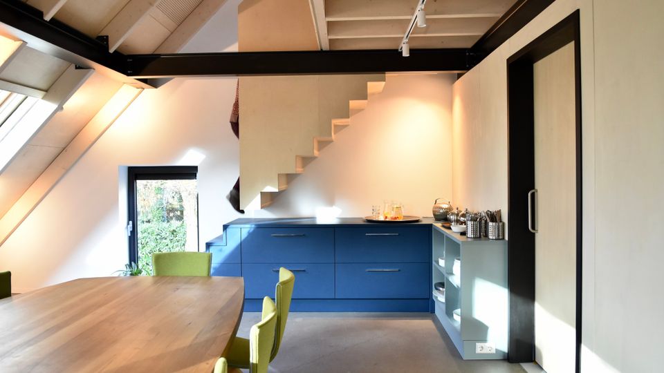 Lichte ruimte onder een schuin dak met tafel en stoelen en een blauwe lage kast.