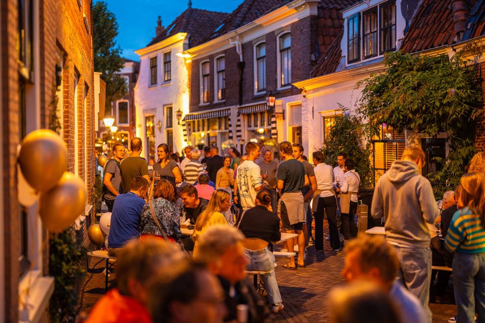 Stedelijk evenement Pracht aan de Gracht in Oudewater, Groene Hart, sfeervol terras met rode lampionnen, live muziek en drukbezochte horeca tijdens zomeravondfestival.