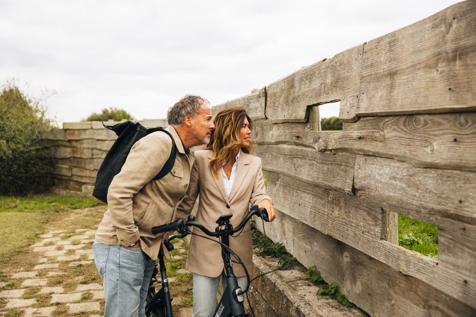 Een man en een vrouw zijn even van de fiets gestapt om door een gat in een kijkwand naar de vogels in het Bargerveen te kijken.