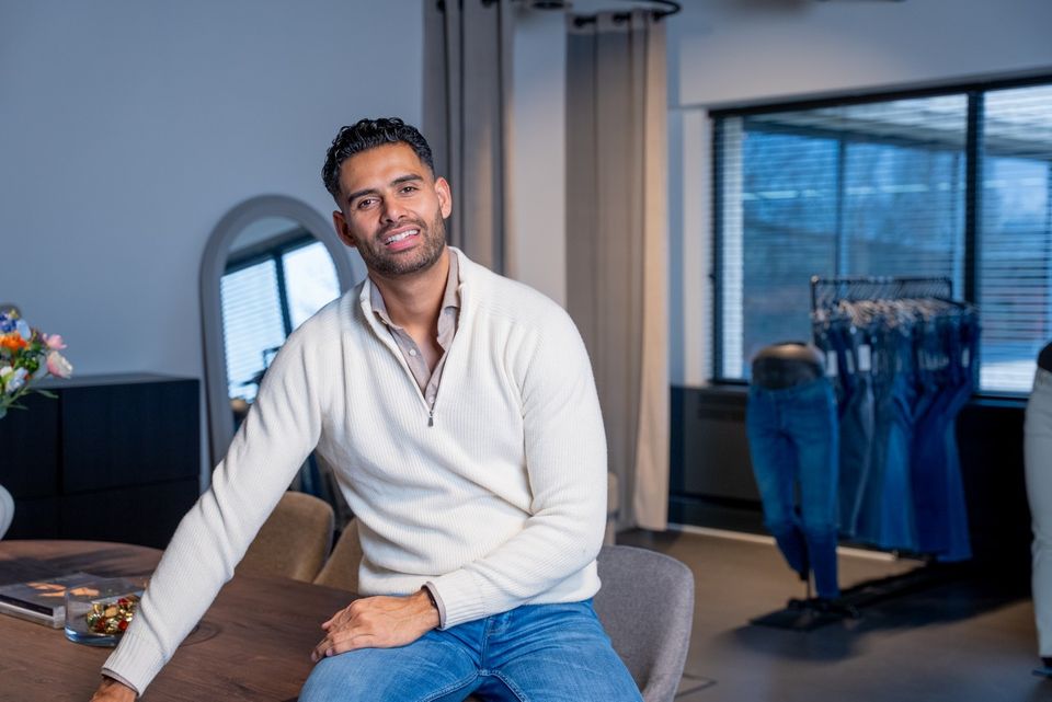 Jeanswinkel Busker Jeans in Woerden, Groene Hart, interieur met een man zittend aan tafel in de winkelruimte met op de achtergrond een presentatie van jeanskleding.