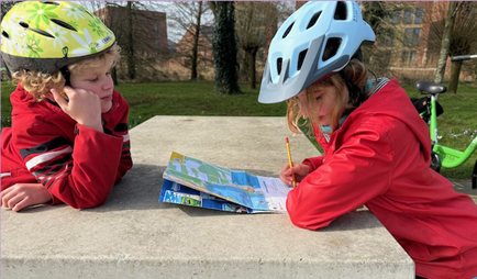 2 kinderen buiten met fietshelm met de speurtocht in hun hand.