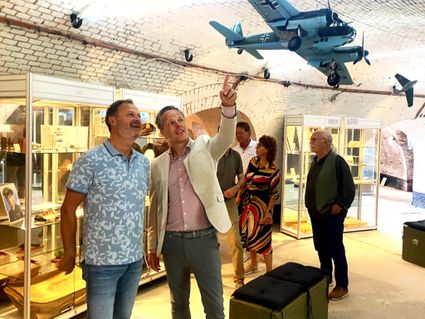 Twee personen staan in een zaal van Museum Sky of Hope, ze wijzen naar een vliegtuigje die aan het plafond hangt.