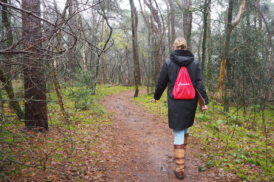 Een vrouw wandelt door het bos met een Drenthetasje op haar rug