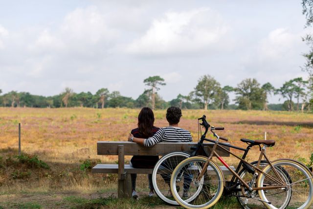 Stel pauzeert tijdens fietstocht op een bankje waar ze genieten van het uitzicht.