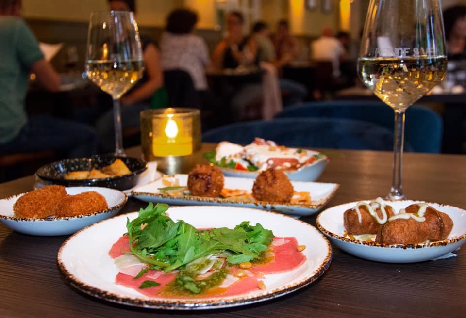 Een tafel gedekt met twee gevulde wijnglazen en borden met eten