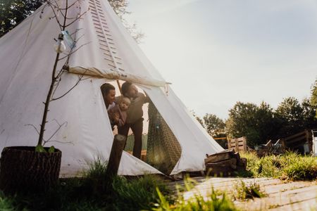 Twee ouders en hun dochtertje kijken vanuit een tipi naar de groene omgeving