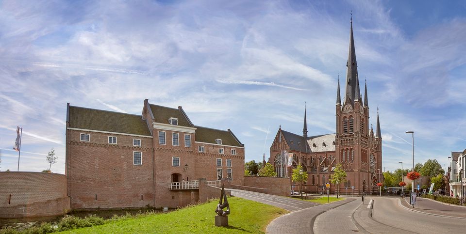 Panoramafoto van Kasteel Woerden en de imposante Bonaventurakerk onder een blauwe lucht met lichte wolken.