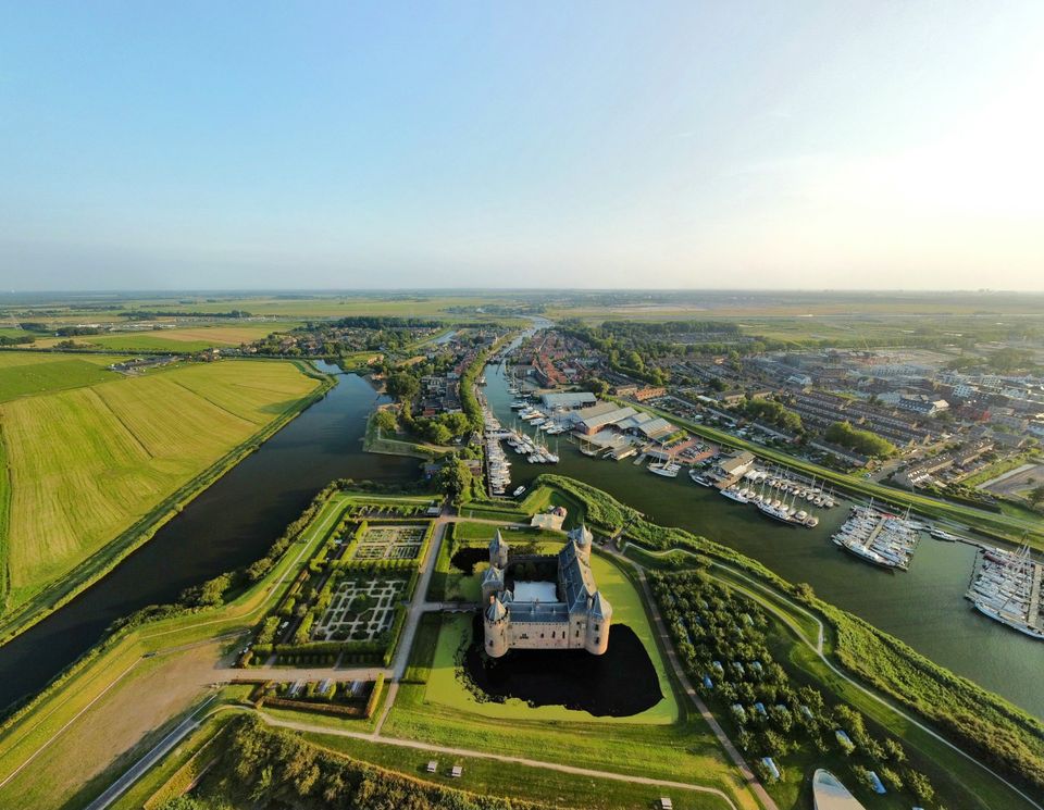 Een foto van kasteel het Muiderslot in Gooise Meren. Dit is een drone-foto. Je ziet niet alleen het kasteel van bovenaf, maar ook vestingstad Muiden, de Vecht en de haven.