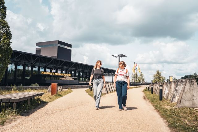 Twee bezoekers wandelen langs het Nationaal Militair Museum in Soesterberg. De foto laat de combinatie van militair erfgoed, architectuur en recreatie zien.