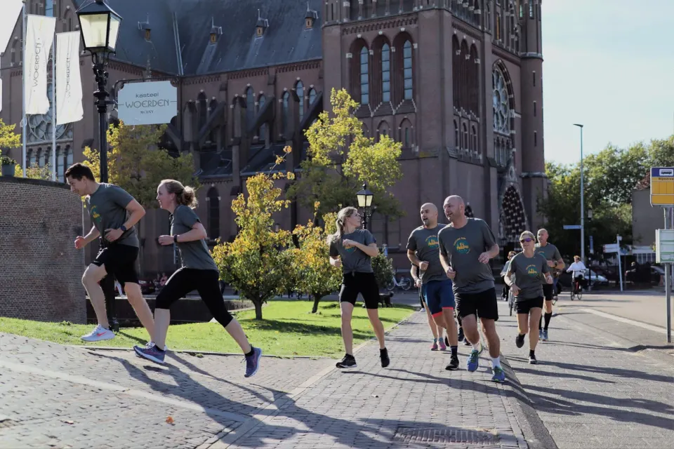 Groep hardlopers tijdens de Culture Run in Woerden, rennend langs Kasteel Woerden in het historische stadscentrum op een zonnige dag.