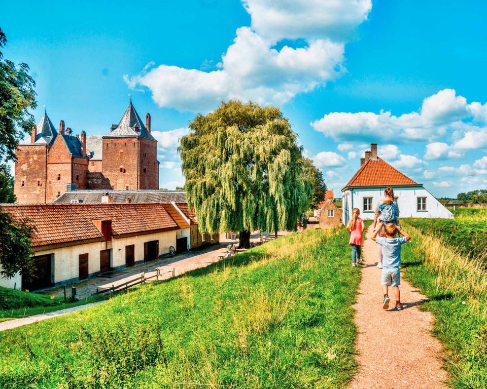 Een gezin wandelt over een wandelpad omgeven door groen. In de achtergrond een oud kasteel.